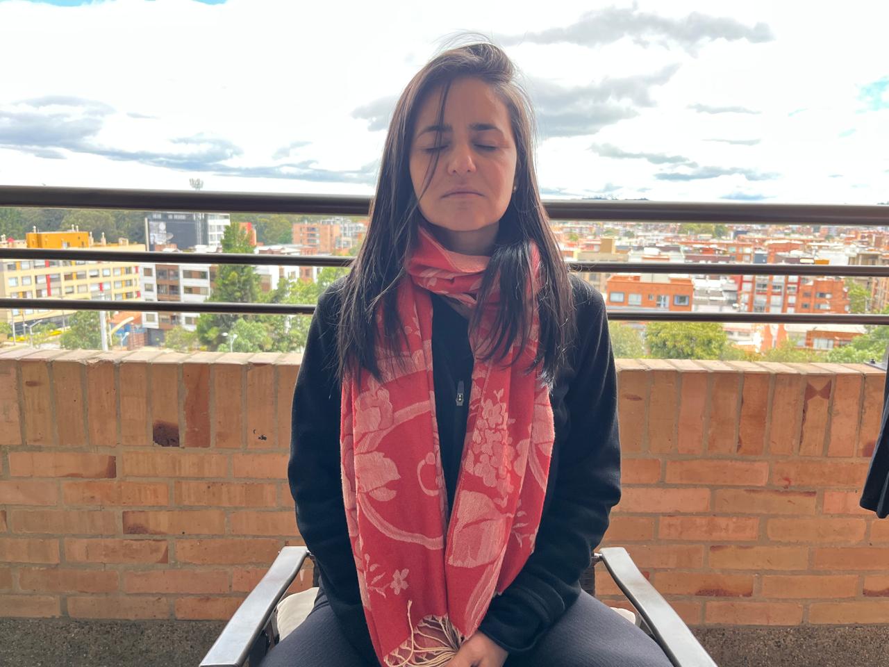 Alejandra meditando con los ojos cerrados en un balcón sobre la ciudad